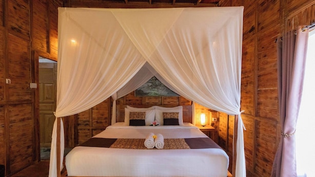 A wooden room with a bed, white canopy, and a painting on the wall. - Room-private Villa Room With Nature View (Ubud)
