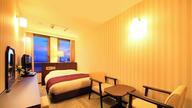 Ein Hotelzimmer mit Bett, Schreibtisch mit Fernseher, Stuhl, kleinem Tisch und einem Fenster mit Vorhängen.