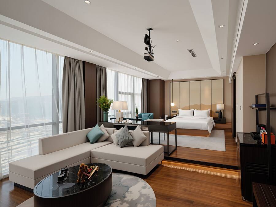 A modern hotel room with a large bed, a sofa, a coffee table, and a desk.