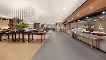 A spacious hotel lobby with a long reception desk, multiple seating areas, and a modern chandelier.