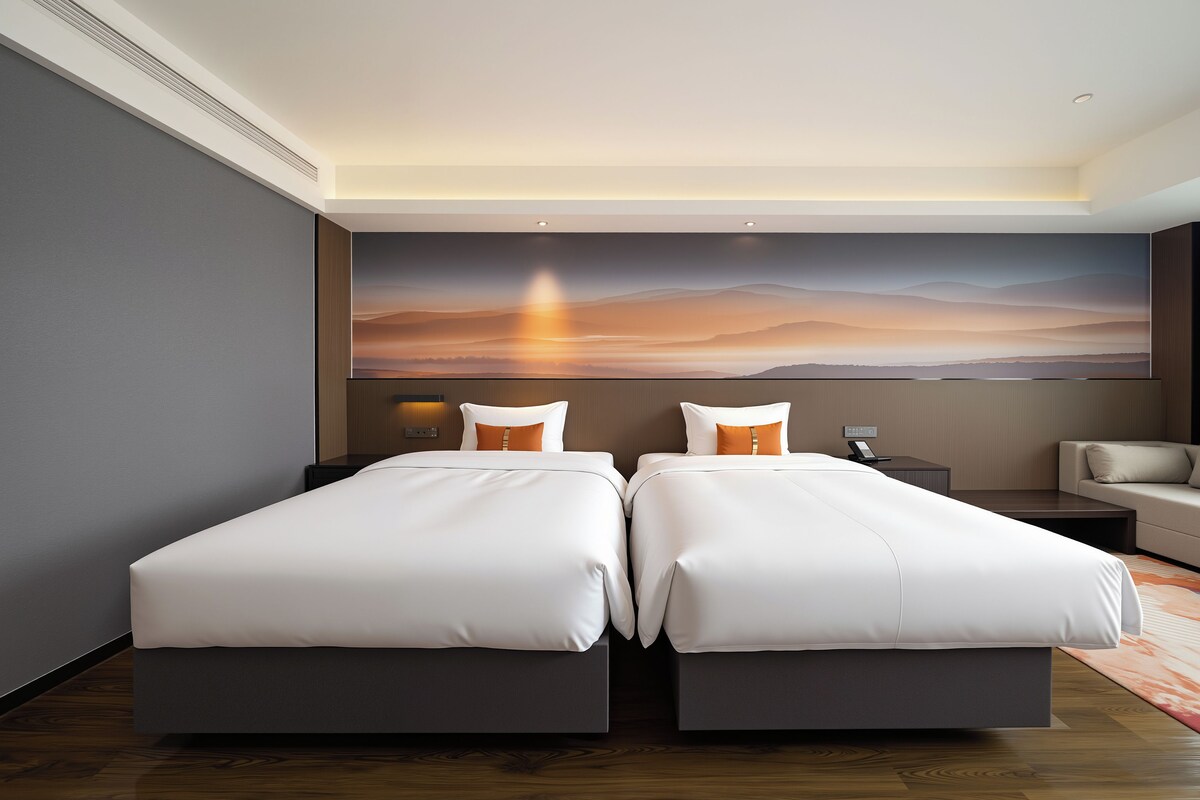 A hotel room with two beds, a desk, a chair, and a large wall mural.