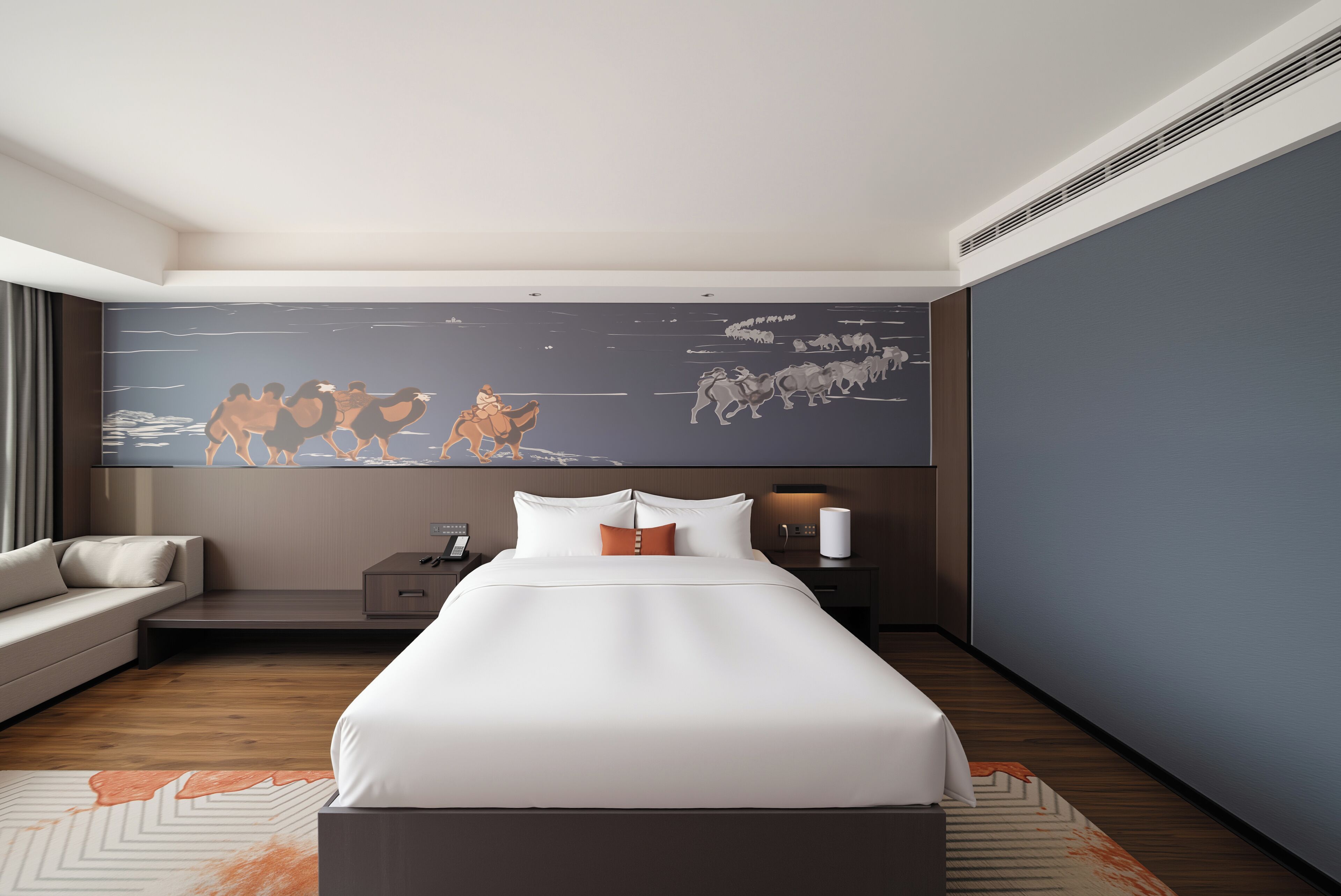A modern hotel room with a large bed, a sofa, a nightstand, and a wall-mounted artwork.
