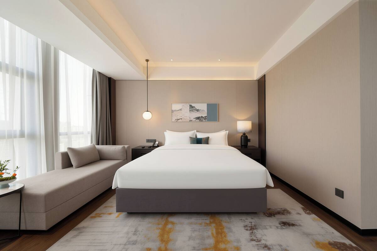 Moderni hotellihuone, jossa on suuri sänky, sohva, yöpöytä ja sivupöytä.