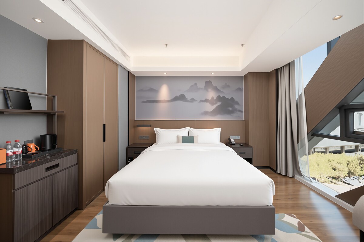A modern hotel room with a large bed, a desk with a computer, a flat-screen TV, and a view of the city.