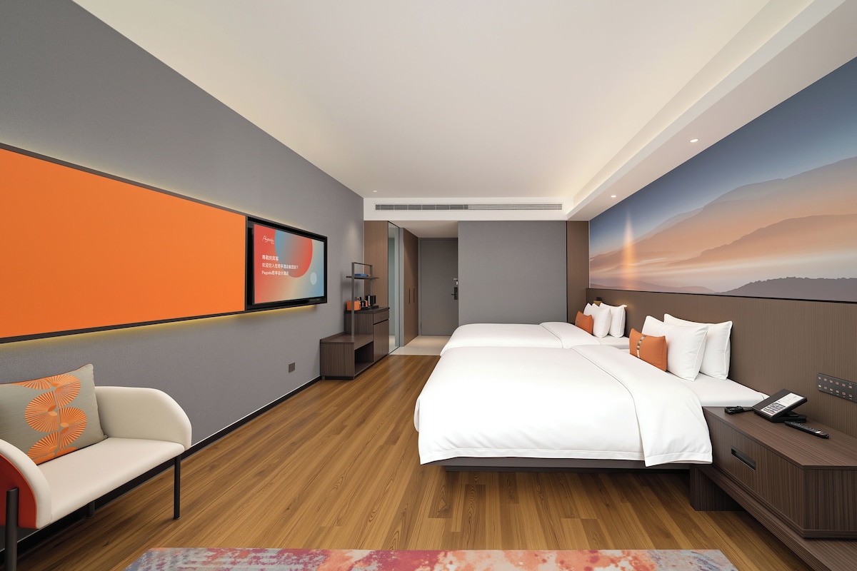 A hotel room with a large bed, a sofa, a desk with a phone, and a painting on the wall.