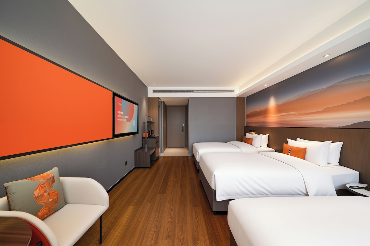 A hotel room with a modern design, featuring a large bed, a sofa, a small table, and a wall-mounted TV.