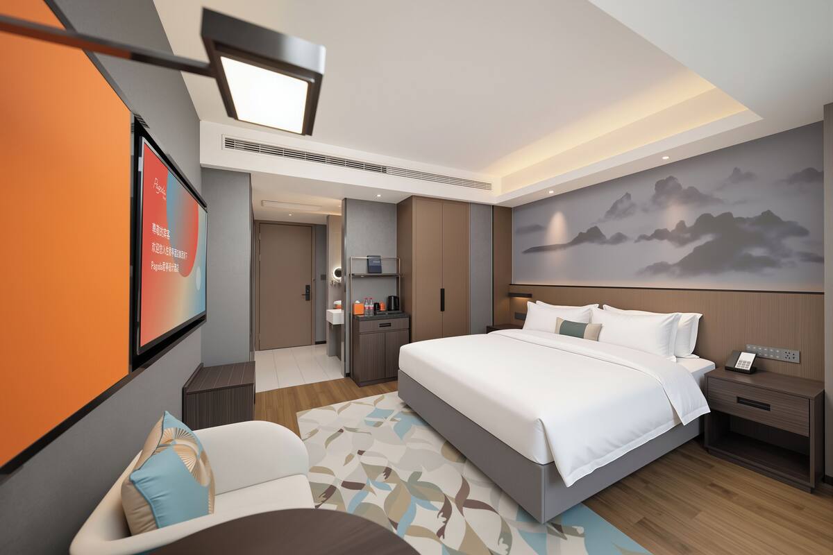 Moderni hotellihuone, jossa on suuri sänky, työpöytä, tuoli, televisio ja seinä, jossa on vuoristomaisema.