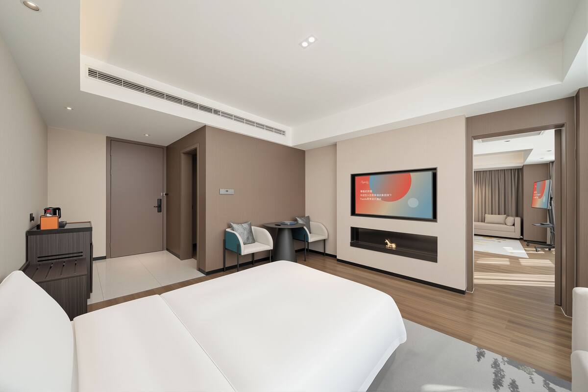 Moderni hotellihuone, jossa on suuri sänky, televisio, työpöytä ja sohva.