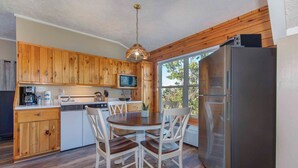 A compact kitchen with wooden cabinets, a stainless steel refrigerator, and a dining table with chairs. - Mountain Jewel - Lake & Mountain View - Romantic Retreat w/ Cozy Space Nook (Sevierville)