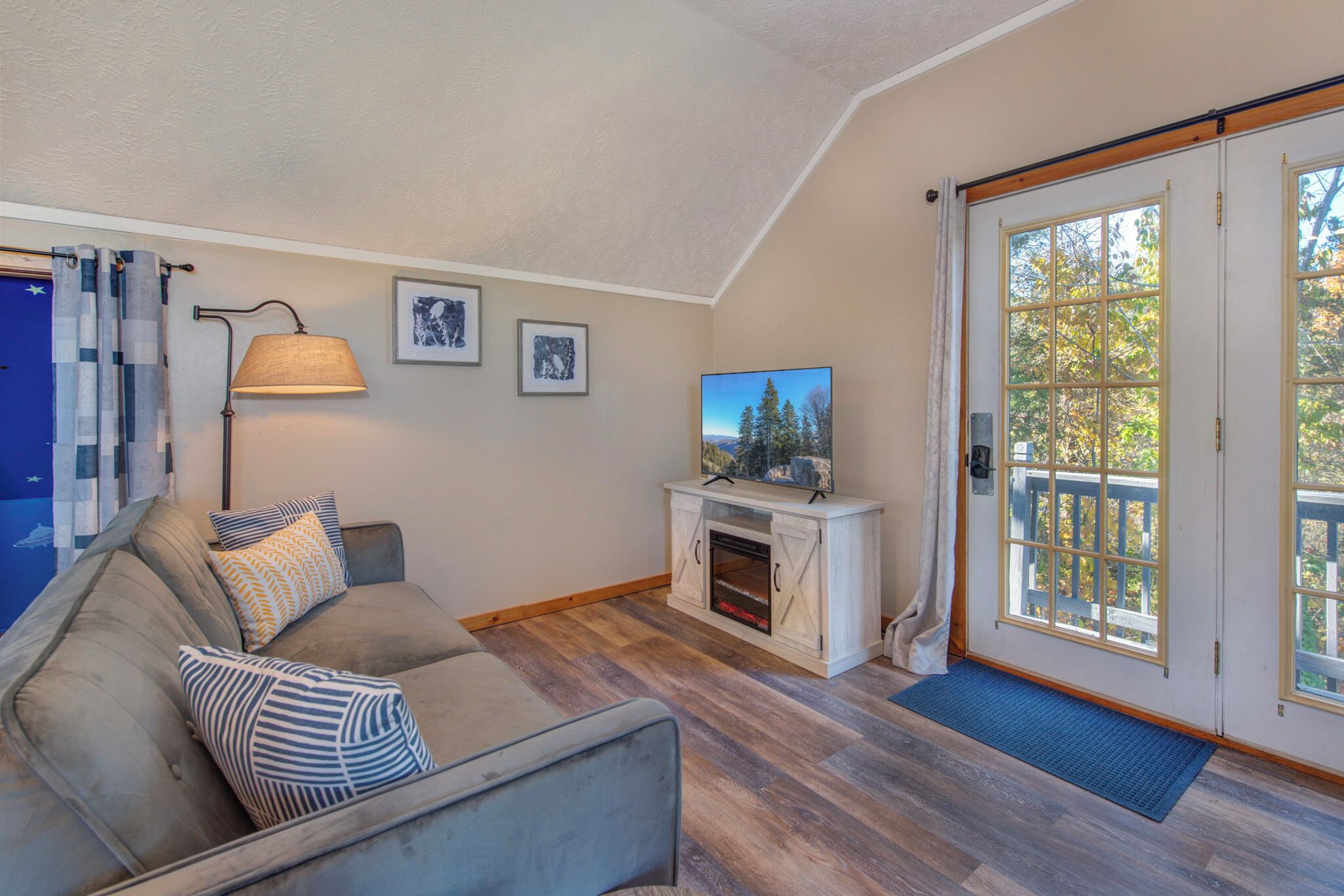 A living room with a sofa, a fireplace, a television, and a door leading to a deck.