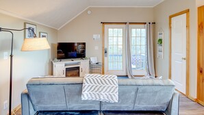 A living room with a sofa, a television, a fireplace, and a view of the outdoors through a sliding glass door. - Mountain Jewel - Lake & Mountain View - Romantic Retreat w/ Cozy Space Nook (Sevierville)
