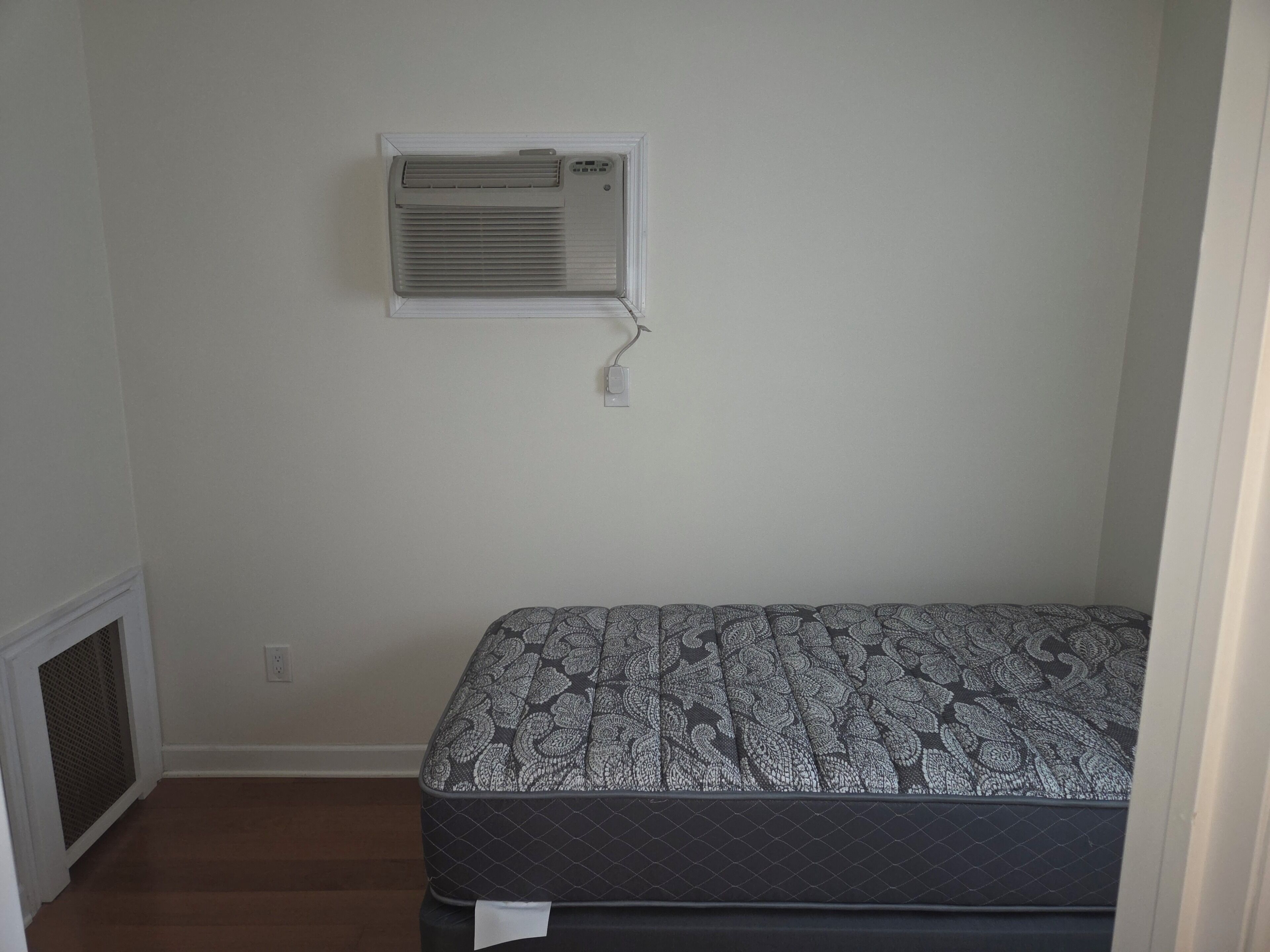 A bedroom with a bed, an air conditioning unit, and a window.