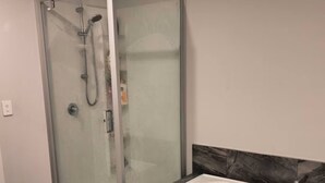 Une salle de bain moderne avec une douche à l’italienne, une baignoire blanche et un pare-baignoire en marbre.