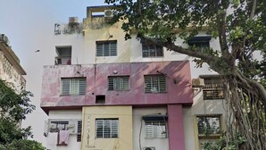 A multi-story building with a pink and beige facade, several windows, and a tree in front. - The Ganapati Abode (Kolkata)