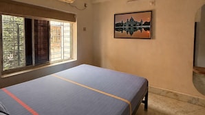 A room with a bed, an air conditioner, a ceiling fan, a window with bars, and a framed picture on the wall. - The Ganapati Abode (Kolkata)