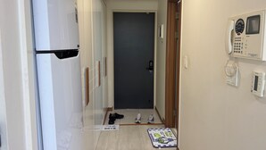 A hallway with a refrigerator, a door, a mat, and a phone on the wall. - Yeoksam Gangnam 5min Cozy Urban Signature Stay (Seoul)