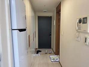 A hallway with a refrigerator, a door, a mat, and a phone on the wall.