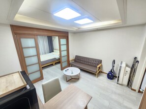 A compact hotel room with a bed, sofa, table, and a small kitchenette area.