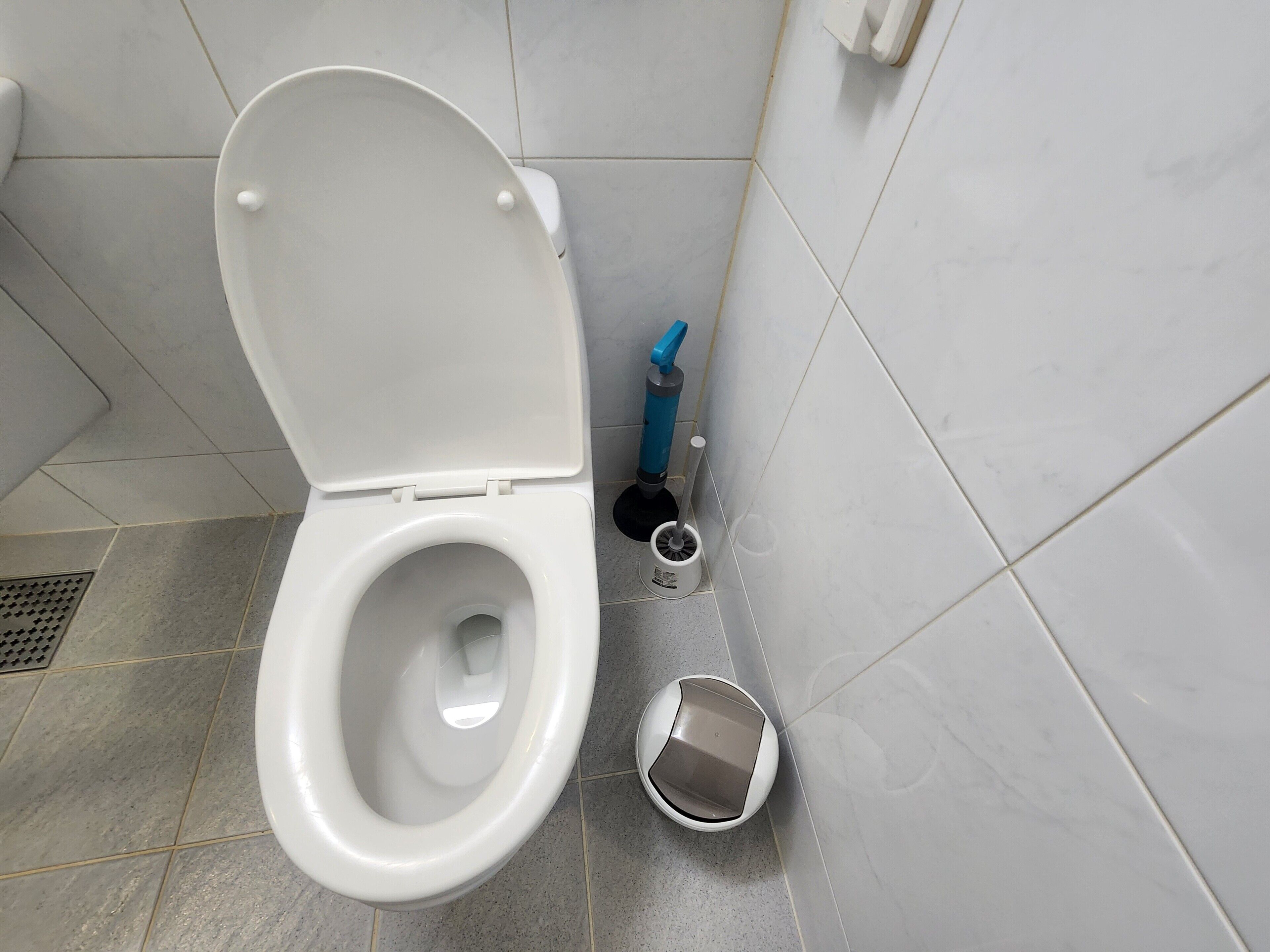 A toilet with a closed lid, a bidet, and a toilet brush in a bathroom with tiled walls and floor.