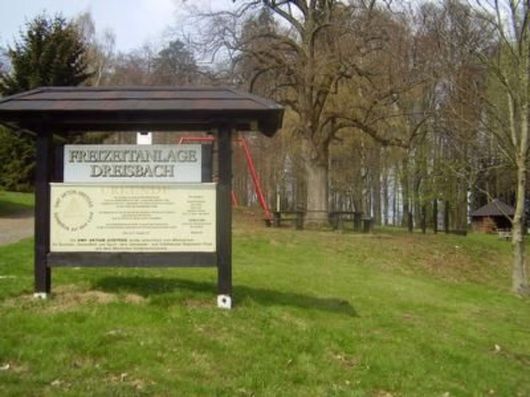 Ein Schild mit Text, eine Rasenfläche und Bäume im Hintergrund.
