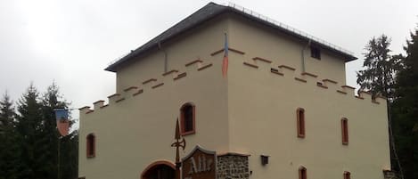 Ein Gebäude mit rustikalem Steingrund und einem hellbeigen Obergeschoss, das einen großen Bogenbogen und zahlreiche Fenster aufweist.
