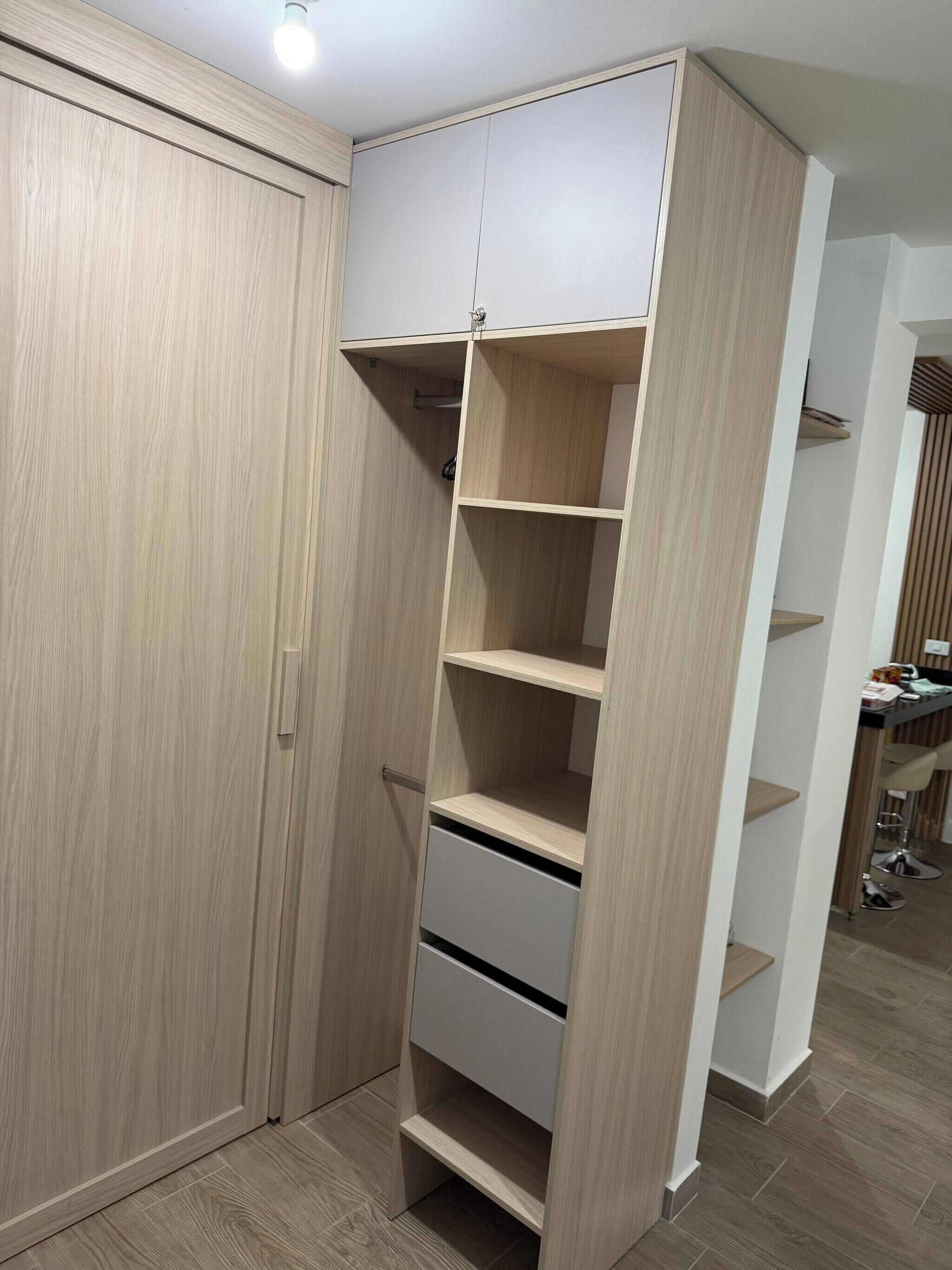 A walk-in closet with multiple shelves and drawers, a hanging rod, and a door with a handle.