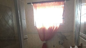 Un bagno con doccia, WC, lavandino e finestra con tende.