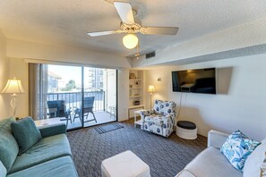 Ein Hotelzimmer mit Deckenventilator, einer Couch, einem Sessel, einem Fernseher, einem Balkon mit Aussicht und einem Bücherregal.