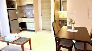Cocina moderna con microondas integrado, refrigerador y pileta. Hay una zona de comedor con una mesa y sillas, y un pequeño banco con toallas.