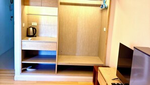 A modern room with a built-in wardrobe, a coffee maker, a TV, and a wooden floor.