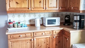 Cozinha com armários de madeira, micro-ondas, cafeteira e diversos utensílios na bancada.