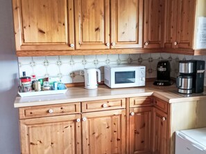 Eine Küche mit Holzausstattung, einer Mikrowelle, einer Kaffeemaschine und verschiedenen Küchenutensilien auf der Arbeitsfläche.