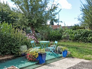 Ein Garten mit einem kleinen Tisch und Stühlen, umgeben von verschiedenen Pflanzen und Blumen.
