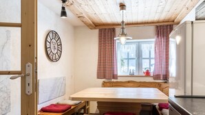 Un interior de madera con una pared de mármol, un reloj, cortinas a cuadros y una mesa de comedor con bancos.