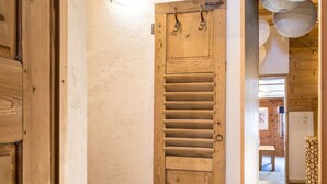 Una puerta de madera con listones horizontales, una pared texturizada y una vista parcial del interior de madera, con un banco y una cortina estampada.