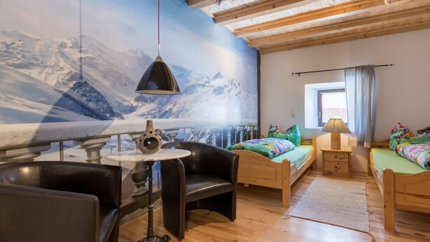 Una habitación acogedora con cama, una silla, una mesa y un mural en la pared de una montaña nevada.