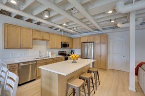 A modern kitchen with stainless steel appliances, wooden cabinets, and a central island with stools.