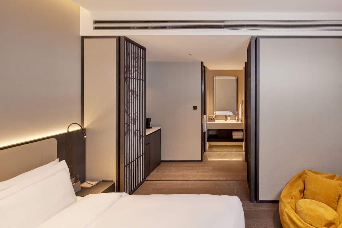 Ein Hotelzimmer mit einem Bett, Nachttisch, Beistelltisch und einem gelben Sessel.