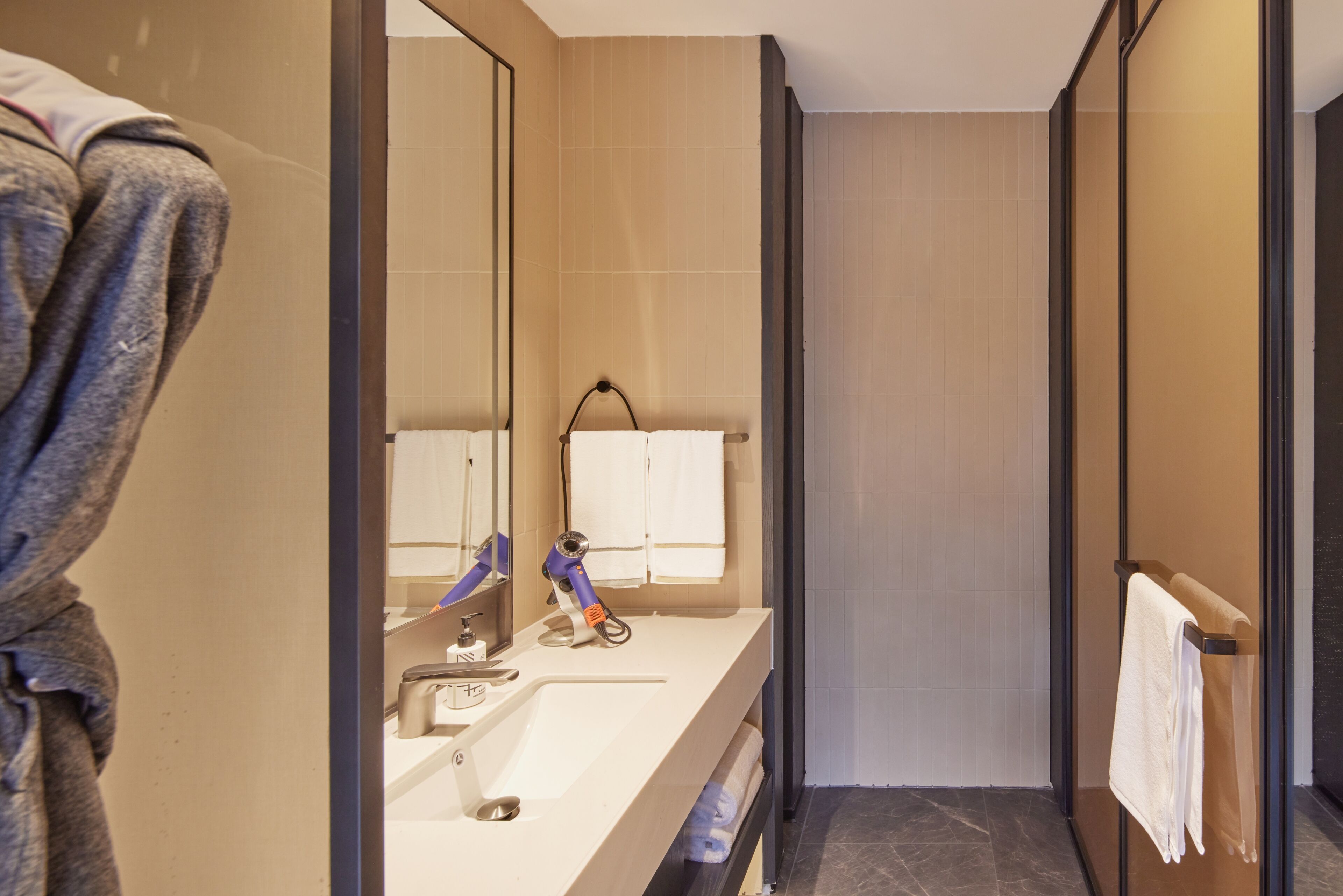A modern bathroom with a large mirror, a sink, a towel rack, and a shower area.