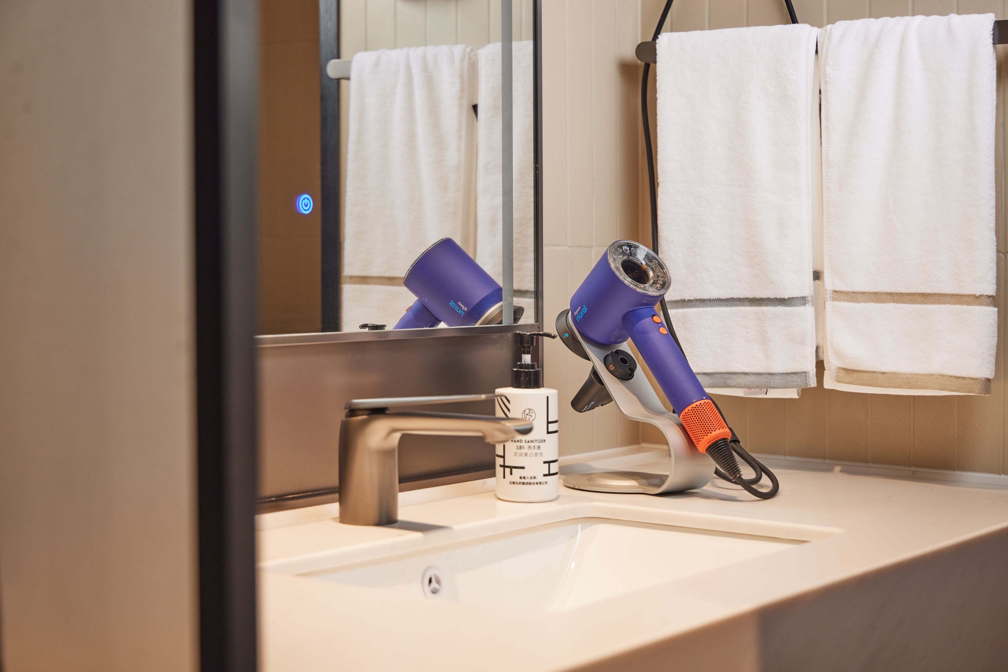 A bathroom with a sink, hand sanitizer, and two hair dryers.