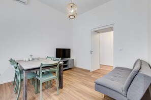 A modern living space with a dining table, chairs, a grey sofa, a television, and a wooden floor. - BMGA | Aurelian 3Bdr 6-Guest Gem (Rome)