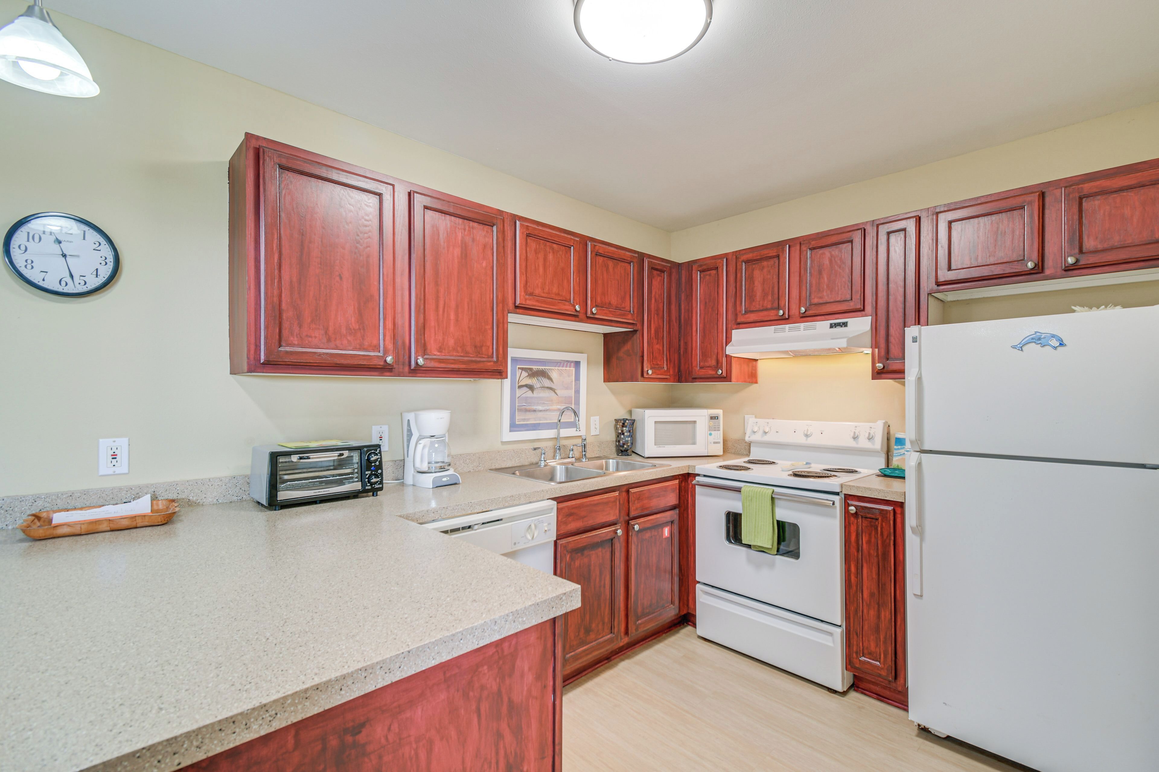 A kitchen with wooden cabinets, a white refrigerator, a microwave, a stove, and a clock on the wall.