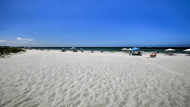 Platja ampla i sorrenca amb ombrel·les i cadiretes de platja, un cel blau clar i un mar tranquil.