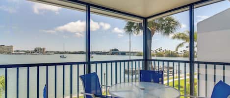 A balcony with a view of a body of water, a table, and chairs.
