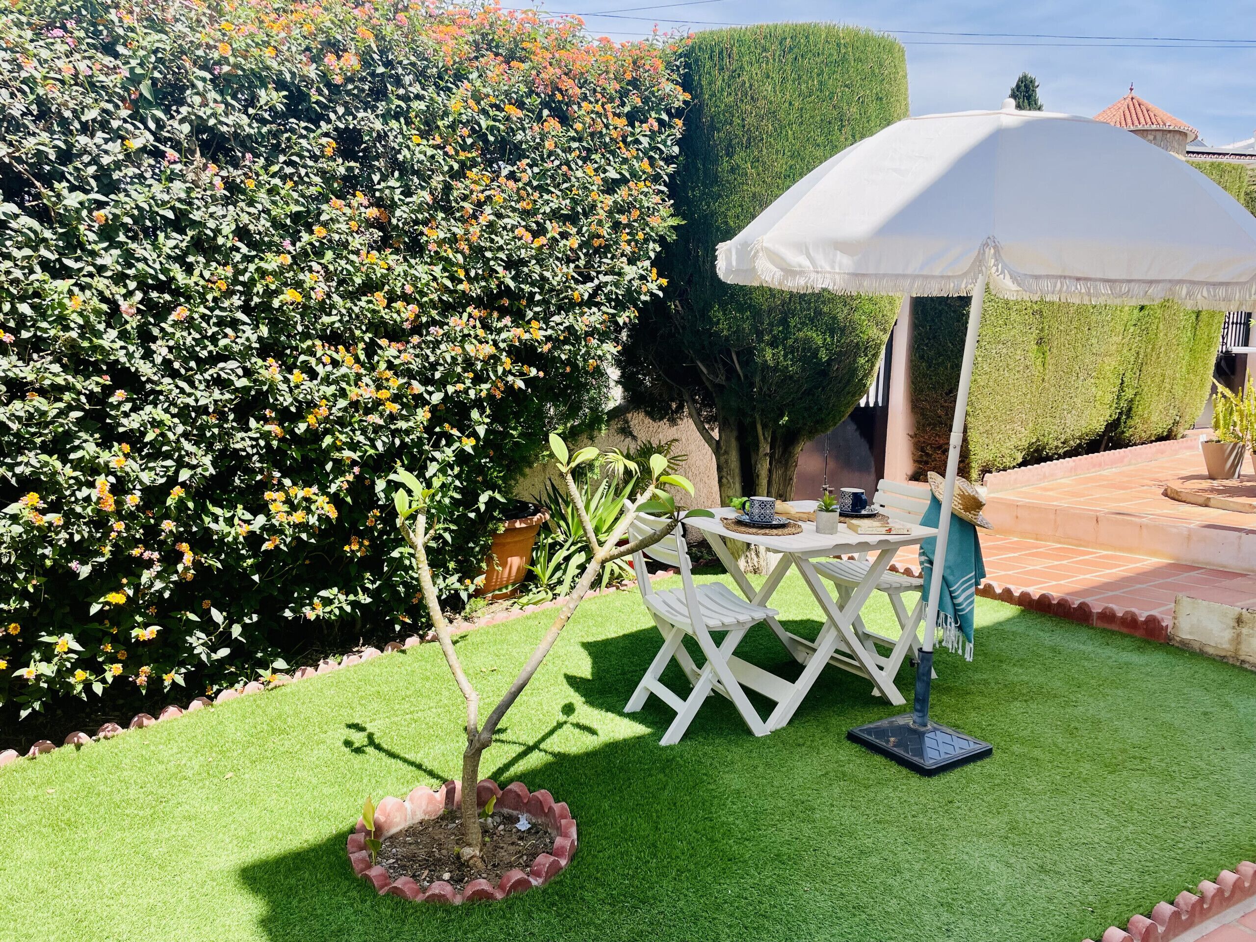 Un patio con sombrilla blanca, una pequeña mesa con sillas y una planta en maceta.