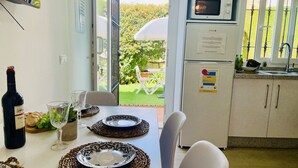 A dining area with a table set for two, a bottle of wine, and a glass. A microwave and refrigerator are visible in the kitchen area. - Apto. Barbacana by At Home Costa del Sol (Caleta de velez)