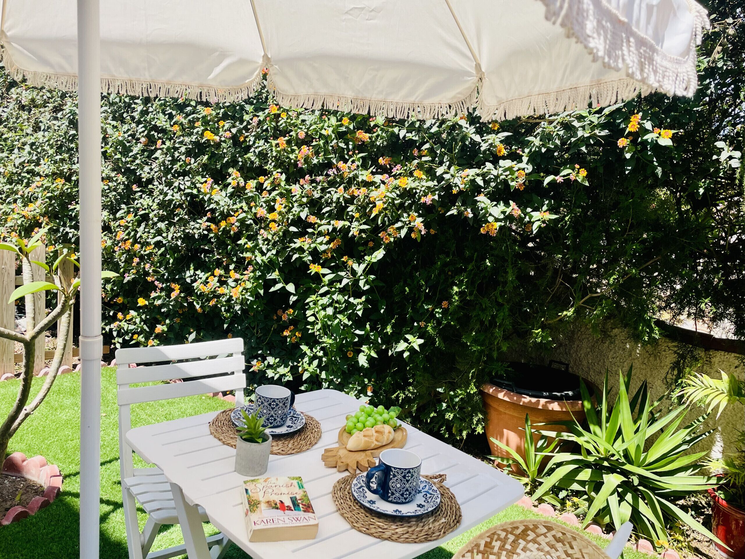 An outdoor patio with a table set for two, featuring a book, a mug, and a plate of bread.
