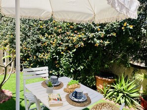 Eine Terrasse im Freien mit einem Tisch für zwei Personen, auf dem ein Buch, eine Tasse und eine Brotschale stehen.