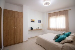 A bedroom with a bed, a wardrobe, a shelf with books and a vase, and a window with curtains. - Apartamento Recreo 10 by At Home Costa del Sol (Torrox)