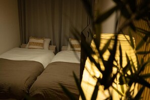 Quarto de hotel com duas camas, uma janela grande e uma planta em primeiro plano.